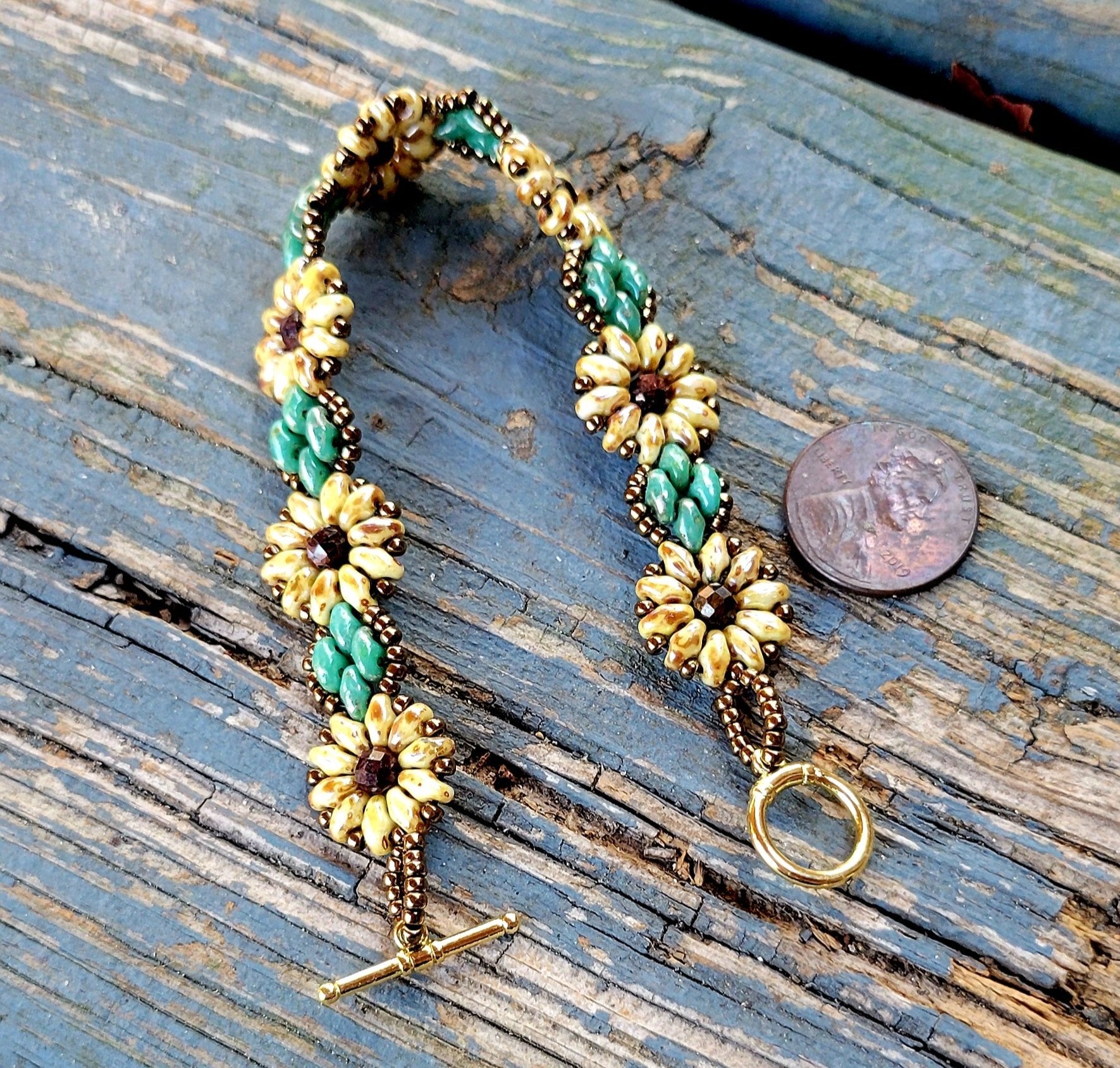 Handmade sunflower bracelet yellow flower green leaf gold toggle clasp shown next to a penny for size